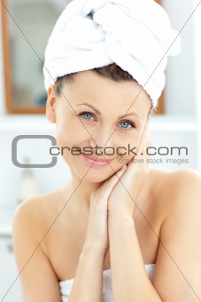 Beautiful young woman with a towel putting cream on her face in 