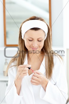 Happy young woman varnishing her fingernails in the bathroom
