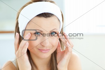 Attractive young woman with a towel putting cream on her face in the bathroom
