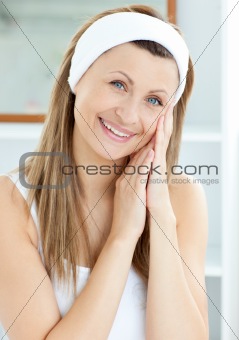 Smiling young woman putting cream on her face in the bathroom