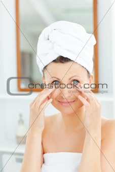 Beautiful young woman with a towel putting cream on her face in 