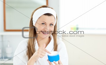 Delighted young woman putting cream on her face in the bathroom