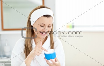 Radiant woman putting cream on her face wearing a headband in th