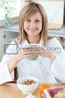 Beautiful woman holding a cup of coffee eating cereals in the ki