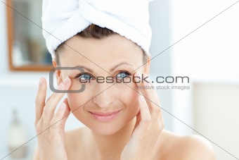 Smiling young woman putting moisturizer on her face  