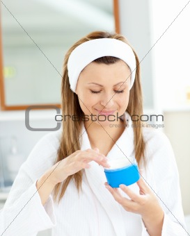 Pretty young woman using cream wearing a bath robe 