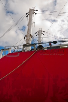 Hull and masts of a red old freighter with pulleys