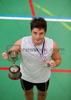 Sporty man holding a cup and a medal standing on a games field