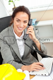 Confident female architect talking on phone and using her laptop