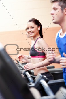 Cute athletic woman with earphones exercising on a running machi