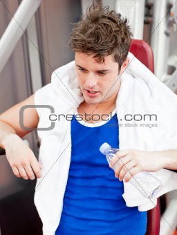 Tired man with a towel and a bottle of water sitting on a bench 