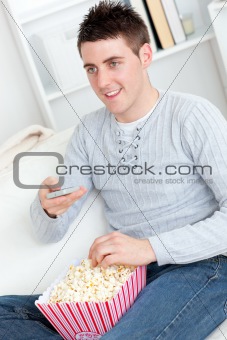 Charming young man eating popcorn watching television in the liv
