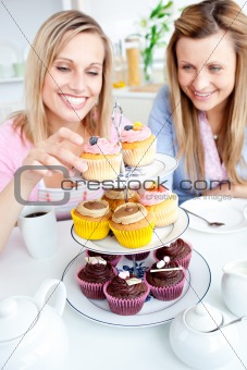 Positive young women eating cakes in the kitchen
