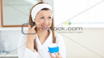Charming young woman using cream wearing a bath robe in the bath