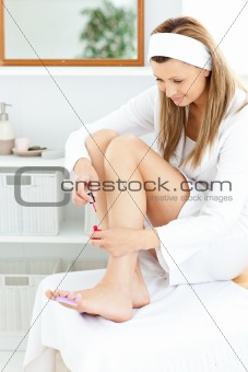 Delighted young woman varnishing her toenails in the bathroom