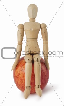 The wooden mannequin sits on a ripe apple