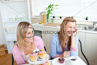 Two cheerful female friends eating pastries and drinking coffee 