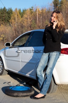 Young woman standing by her damaged car and calling for help