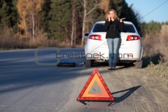 Young woman standing by her damaged car and calling for help
