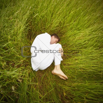 Man lying on grass in fetal position