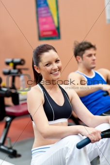 beautiful woman using a rower with her boyfriend in a fitness ce