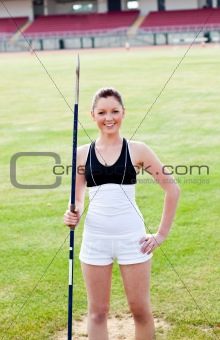 joyful sporty woman holding a javelin standing in a stadium