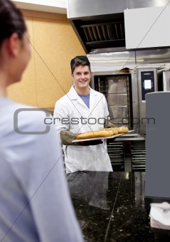 Cheerful baker showing his baguettes to a female customer in his