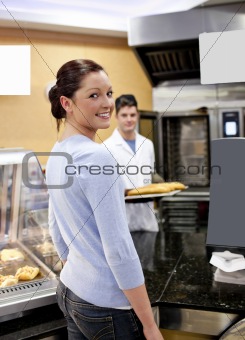 Attractive woman buying baguette in a cafeteria with baker in th