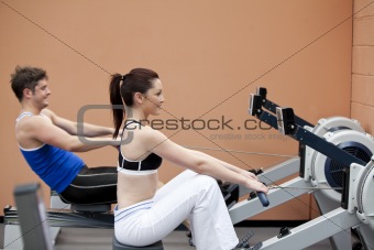 Young couple using a rower in a sport centre