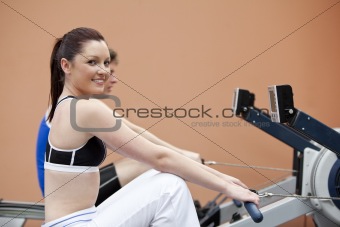 Happy woman with her boyfriend using a rower in a fitness centre