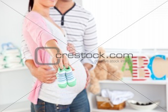 Close-up of a bright pregnant woman holding baby shoes while hus