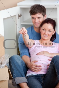portrait of future parents looking at key sitting on the floor