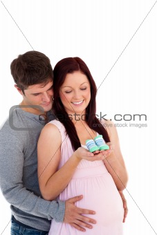young future parents looking at baby shoes against a white backg