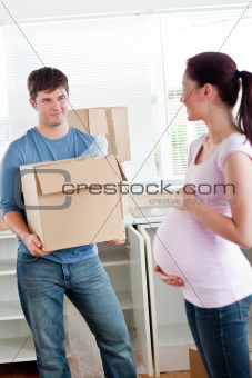 smiling man with cardboard looking at his pregnant wife standing