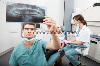 Dentist checking x-ray with assistant and patient in the background