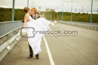 Groom carries his bride in his arms on bridge