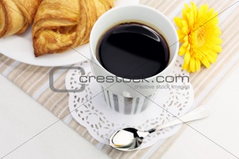 A cup of black coffee and croissants