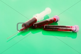Medical test tubes and syringe with blood on green
