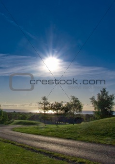 Sunrise sunburst over sea and grassy foreground and road
