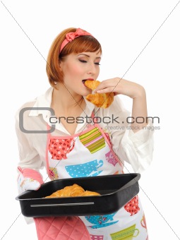 Beautiful cooking woman in apron eating fresh made croissant 