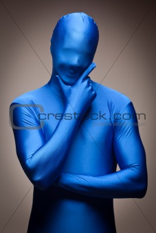 Thinking Man with Hand on Chin Wearing Full Blue Nylon Bodysuit on a Grey Background.
