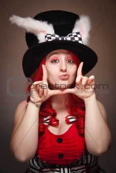 Attractive Red Haired Woman Wearing Bunny Ear Hat and Framing Her Face with her Hands on a Grey Background.