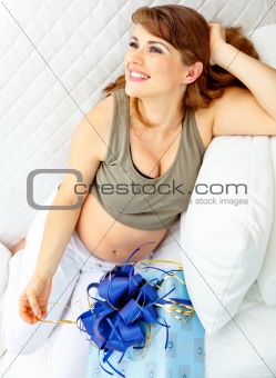 Smiling  beautiful pregnant woman sitting on sofa with present for her  unborn baby
