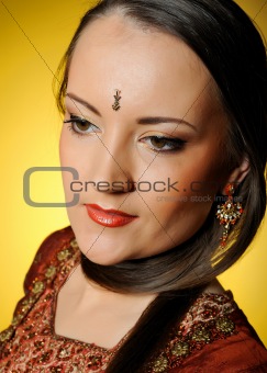 Young beautiful woman in indian traditional jewellary, bindi and sari dress. yellow background
