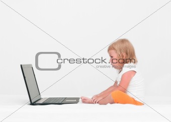 A small child is sitting with a laptop on the bed