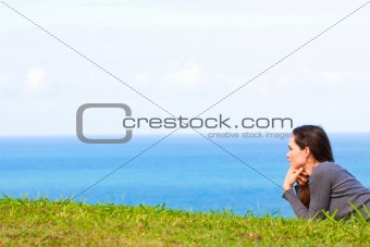 A sad and depressed young woman lying in the green grass by the ocean