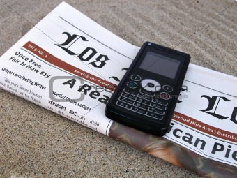 Close up shot of celphone and newspaper on the sand