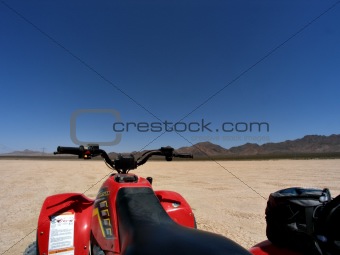 ATV on dry lake bed against mountains and clear blue sky