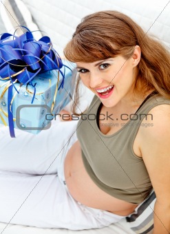 Smiling  beautiful pregnant woman sitting on couch with present for her  unborn baby
