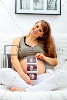 Smiling  beautiful pregnant  woman sitting on sofa with echo in hand.
